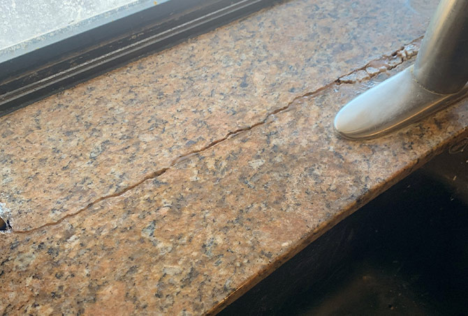 This image shows a crack in a granite countertop behind the sink faucet.